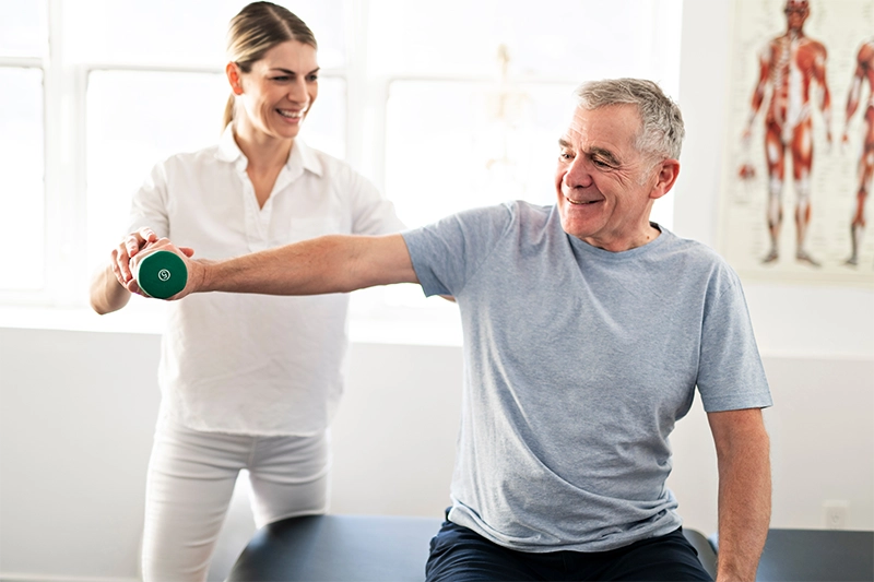 A physical therapist assists an elderly man with arm exercises, highlighting high-quality, patient-focused care and outcome-driven therapy solutions at Pivot Rehabilitation. Experienced clinicians deliver personalized physical therapy services to enhance patient outcomes.