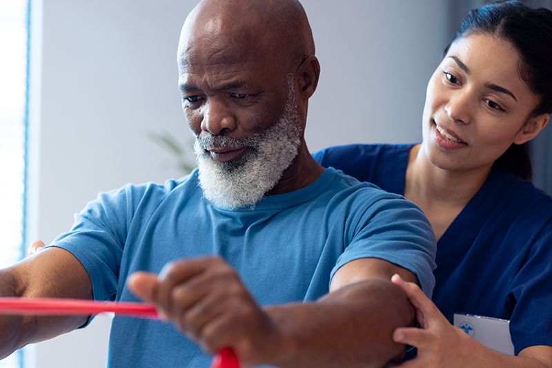 A physical therapist assists an elderly man with resistance band exercises, demonstrating the comprehensive therapy solutions offered by Pivot Rehabilitation. The focus is on delivering high-quality, patient-centered care and achieving excellent therapy outcomes.